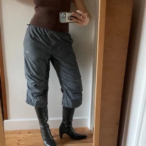 Nike Capris  - Säljer ett par grå Capris / trekvartsbyxor från Nike i bra skick. De har en loose passform och sitter otroligt bekvämt. Byxorna har en elastisk midja och är tillverkade i ett syntetmaterial som andas bra. Perfekta för höst och vår!