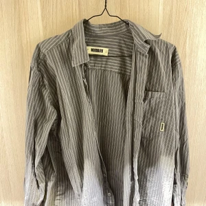 Grå randig skjorta från Woodbird - Säljer en snygg grå skjorta från Woodbird i storlek M. Skjortan har ett stilrent randigt mönster och är långärmad. Perfekt för både vardag och fest! Den är i bra skick och redo för en ny ägare. Passar perfekt till jeans eller chinos för en avslappnad look.