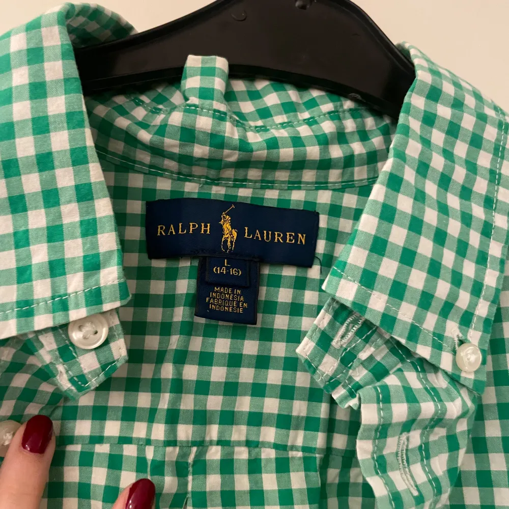 Säljer en snygg grön och vit rutig skjorta från Ralph Lauren i mycket bra skick. Skjortan har långa ärmar och knappar framtill. Den är perfekt för både vardag och festliga tillfällen. Broderad logga i rosa på bröstet ger en extra touch av stil. Passar perfekt för vår och sommar!. Skjortor.