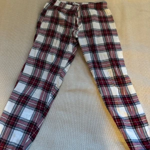 Rutig byxa i bomull - Säljer ett par mysiga rutiga byxor i bomull. De har en skön passform och är perfekta för avslappnade dagar hemma. Färgerna är en mix av rött, vitt och svart, vilket ger en klassisk look. Byxorna har resår i midjan för extra komfort.