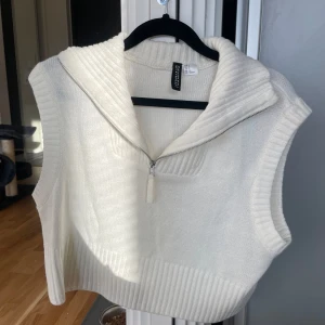Vit stickad väst från H&M - Säljer en superfin vit stickad väst från H&M. Den har en dragkedja framtill och en mysig krage. Perfekt för lager-på-lager under höst och vår. Västen är i mycket bra skick och passar perfekt till både vardag och fest.