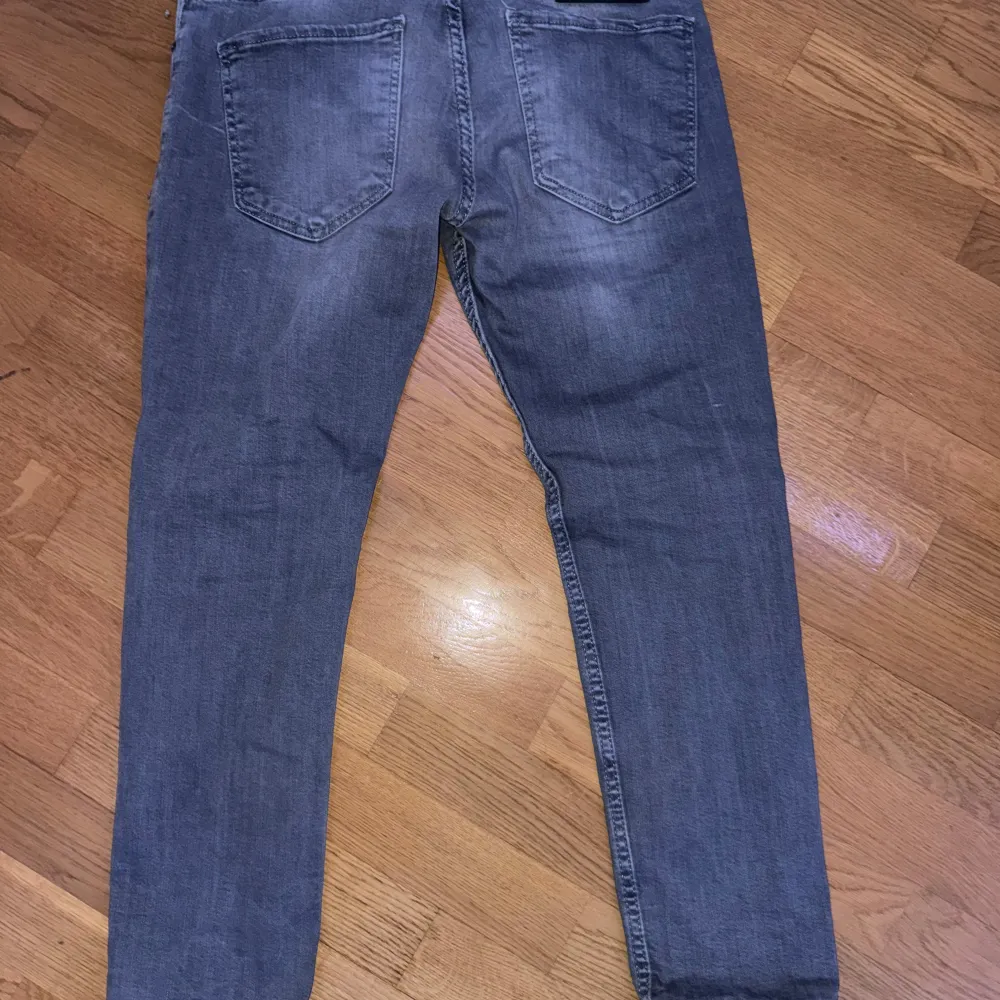 Säljer ett par grå jeans från Dsquared2 i bra skick. De har en cool, sliten look med små revor och en bekväm passform. Perfekta för en avslappnad stil. Midjan är normal och de har klassiska fem fickor. längden är runt 90cm och bredden 44cm!. Jeans & Byxor.