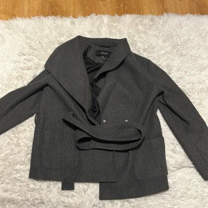 Grå kappa från Vero Moda - Säljer en snygg grå kappa från Vero Moda i storlek L. Den har en stilren design med bälte i midjan och långa ärmar. Perfekt för höst och vår! Kappan är i mycket bra skick och passar både till vardags och fest.