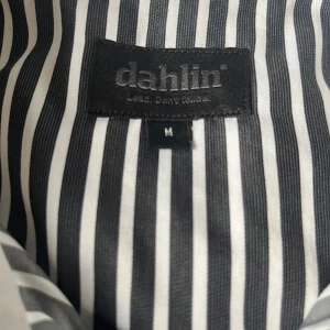 Randig skjorta från Dahlin - Snygg och stilren randig skjorta från Dahlin i svart och vit. Skjortan har en klassisk krage och knappar framtill. Perfekt för både vardag och festliga tillfällen. Den är långärmad och har en bröstficka för extra stilpoäng. Passar perfekt till både jeans och kostymbyxor!