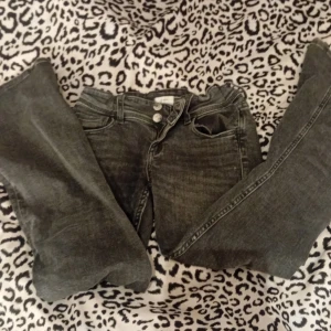 Grå jeans från Gina Tricot - Säljer ett par grå jeans från Gina Tricot i storlek 152. De har en klassisk femficksdesign med knappar fram och bakfickor med knappdetaljer. Perfekta för vardagsbruk och passar till det mesta. Skicket är bra och de är bekväma att bära.