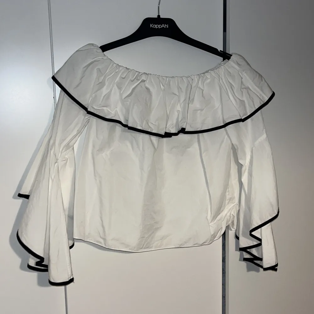 Snygg vit offshoulder blus från ZARA med volangdetaljer och svarta kanter. Perfekt för fester eller en stilren vardagslook. . Toppar.