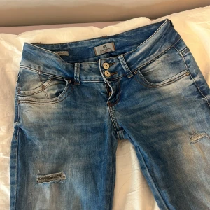 Blå jeans från LTB - Säljer ett par snygga blå jeans från LTB i bra skick. De har en cool slitning på framsidan och dubbla knappar i midjan. Perfekta för en avslappnad vardagslook. Passar bra till både sneakers och boots!