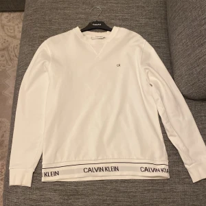 Vit långärmad tröja från Calvin Klein - Säljer en stilren vit långärmad tröja från Calvin Klein. Den har en diskret CK-logga på bröstet och ett elastiskt band med Calvin Klein-text vid nederkanten. Perfekt för en avslappnad men ändå snygg look. Inga skador, använd en eller två gånger, helt fläckfri. 