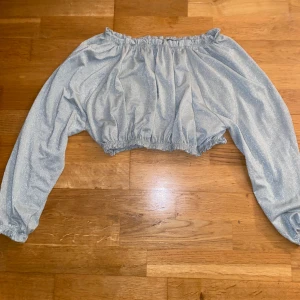 Glittrig offshoulder topp från Bik Bok - Säljer en superfin glittrig offshoulder topp från Bik Bok i storlek S. Perfekt för festliga tillfällen! Den har  en elastisk kant vid axlar och midja för en bekväm passform. Toppen är i ett skimrande grönt/silvermaterial som verkligen fångar ljuset. Köpt för ett tag sedan men endast använd ett fåtal gånger då den var lite kort i armarna för mig.
