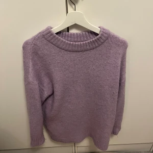 Ljuslila stickad tröja - Mysig ljuslila stickad tröja i mjukt material. Perfekt för kyliga dagar med sin varma och bekväma passform. Tröjan har långa ärmar och en ribbad rund halsringning. Passar både till vardags och mysiga hemmakvällar. 🧶💜