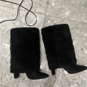 Svarta pälsboots med klack - Säljer ett par svarta boots i syntetpäls med klack. Perfekta för vintern med sin varma och mysiga design. De har en stilren look som passar både till vardags och fest. Skorna är i mycket bra skick och redo för nya äventyr! Hälen gick sönder en gång men har limmat tillbaka den så borde funka bra!