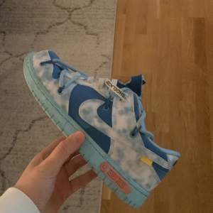 Säljer ett par snygga Nike sneakers i blått och vitt med coola detaljer. Skorna har en unik design med snörning och en tydlig Nike-logga på baksidan. Perfekta för att sticka ut i mängden! 🌀