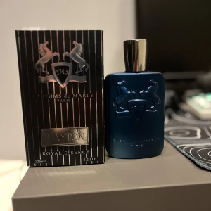 Parfym Parfums de Marly Layton - Säljer en lyxig parfym från Parfums de Marly, modellen Layton. Flaskan är elegant i en djupblå färg med en stilren design och ett silverfärgat lock. Förpackningen är svart med silverdetaljer och har en kapacitet på 125 ml. Perfekt för den som vill ha en sofistikerad doft med en touch av elegans.
