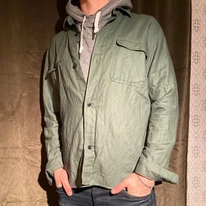 Grön overshirt från Dressmann - Säljer en snygg grön overshirt från Dressmann i linneblandning. Perfekt för lager-på-lager-stil med två bröstfickor och knappar framtill. Knappt använd! Vid minsta fråga eller fundering hör av er🤝