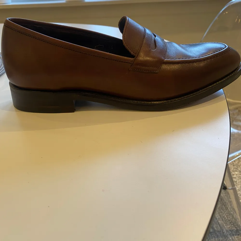 Säljer ett par stilrena bruna loafers från Loake1880 i skinn. De är i mycket bra skick och perfekta för både vardag och fest. Tillverkade i England med hög kvalitet och klassisk design. Passar perfekt för höst och vår!. Skor.