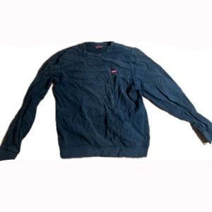 Mörkblå tröja från Supreme - Säljer en mörkblå tröja från Supreme i bra skick. Den har en klassisk design med rund hals och långa ärmar. Perfekt för en casual look eller streetwear-stil. Supreme-loggan är broderad på bröstet. Passar perfekt till höst och vår!