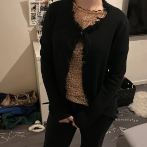 Svart kofta med spetsdetaljer - Säljer en elegant svart kofta med spetsdetaljer längs kanterna. Perfekt för både vardag och fest! Den har långa ärmar och en fin passform som ger en stilren look. Passar bra över en blus eller topp för att ge en extra touch till din outfit. 🖤