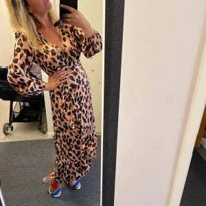 Leopardmönstrad långklänning - Säljer en supercool leopardmönstrad långklänning med omlott-design. Klänningen har långa ärmar och en v-ringad hals, perfekt för både fest och vardag. Materialet känns mjukt och bekvämt, och den har en snygg volangdetalj längst ner. Perfekt för dig som vill sticka ut!Helt ny