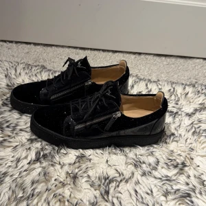 Svarta sneakers med dragkedja - Snygga svarta sneakers i mycket bra skick med glittrig yta och dragkedja på sidan. De har en stilren design med snörning och en bekväm passform. Perfekta för både vardag och festliga tillfällen!