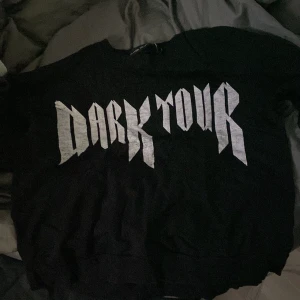 Svart tröja från The Black Label Collection - Cool svart tröja med texten 'Dark Tour' i en rockig stil. Perfekt för en avslappnad look eller konsertkvällar. Tröjan är i bra skick och har en normal passform. Ett måste för alla som älskar svart och edgy mode!