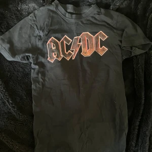 Svart AC/DC t-shirt - Säljer en svart AC/DC t-shirt i bomull. Köpt på humana second hand. Den har ett tryck av bandets logga på framsidan.
