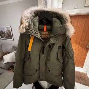 Grön vinterjacka från Parajumpers - Säljer en grön Parajumpers vinterjacka i slim fit. Jackan har en fluffig pälsfodrad huva och flera praktiska fickor. Den är perfekt för kalla vinterdagar och har snygga detaljer som dragkedja och knappar. Passar både för vardag och äventyr! 🧥❄️