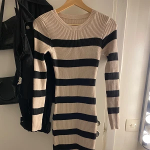 Randig stickad klänning - Säljer en superfin randig stickad klänning i beige och svart. Den är långärmad och har en tight passform som verkligen framhäver figuren. Perfekt för höst och vinter, och den är både bekväm och stilren. Passar lika bra till vardags som till festligare tillfällen! Klänning är helt ny och aldrig använts 💞💞