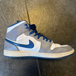 Nike Air Jordans i grått och blått - Säljer ett par Nike Air Jordans i grått och blått. Skorna har en klassisk hög design med snörning och är i bra skick. Perfekta för både vardag och sportiga tillfällen. De har en snygg kombination av grått och blått med vita detaljer.