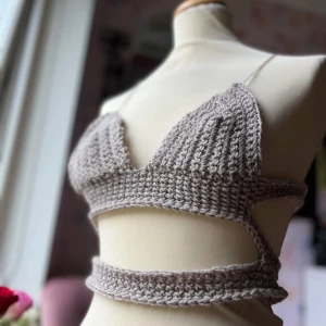 Beige virkad topp - Säljer en superfin beige virkad topp med smala axelband och en unik design med omlott och knytning runt midjan. Perfekt för sommardagar eller en avslappnad fest. Toppen är croppad och ger en bohemisk känsla. Passar perfekt till höga jeans eller en kjol.