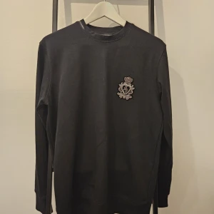 Svart tröja från Dolce & Gabbana - Säljer en stilren svart tröja från Dolce & Gabbana i bomull. Den har en snygg broderad detalj med en krona och hjärta på bröstet. Perfekt för både vardag och fest. Tröjan är i mycket bra skick och passar perfekt till höst och vinter.