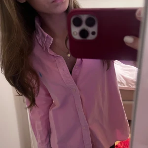 Rosa skjorta från Ralph Lauren - Säljer en snygg rosa skjorta från Ralph Lauren i storlek M. Skjortan har en klassisk krage och knappar framtill. Den är långärmad och har det ikoniska Ralph Lauren-logotypen broderad på bröstet. Perfekt för både vardag och fest! 💖Aldrig använd!!!