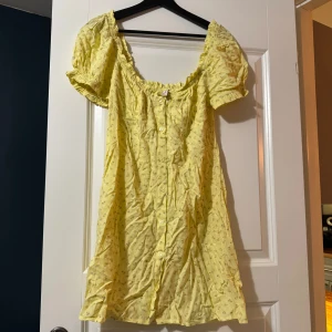Gul kortärmad klänning - Söt gul klänning med korta ärmar och knappar framtill. Perfekt för sommardagar med sitt lätta och luftiga material. Den har en smickrande passform och ett diskret mönster som ger en extra touch. Perfekt för en avslappnad dag ute i solen!