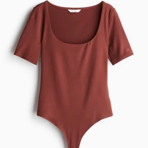 Brun bodysuit - Snygg brun bodysuit med korta ärmar och rund halsringning. Perfekt för både vardag och fest. Materialet är mjukt och stretchigt för en bekväm passform.