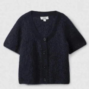 Kortärmad kofta från COS - Säljer en supermjuk och stilren svart kofta från COS. Storlek m men passar bra på XS-M. Den har korta ärmar och knappar framtill, perfekt för både vardag och fest. Koftan är i mohair som ger en lyxig känsla. Passar perfekt till jeans eller kjol! Bilderna är från tidigare ägaren. 