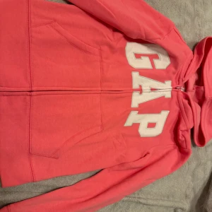 Rosa hoodie från GAP Kids - Säljer en superfin rosa hoodie från GAP Kids i storlek XL (12) som jag skulle säga är  146/152  Den har en dragkedja framtill och en stor logga på fram sidan helt ny endast tästad katt fins i hemmet skriv för mer info.💞⚠️endast swish!!!⚠️