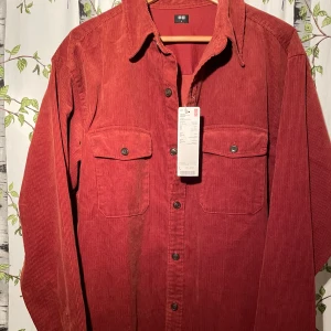 Röd/orange manchester overshirt från Uniqlo - Säljer en snygg orange manchester overshirt från Uniqlo i storlek L. Skjortan har två bröstfickor med knappar. Perfekt för höst och vår, och den är i nytt skick med etikett kvar. Passar både till vardags och lite mer uppklädda tillfällen.