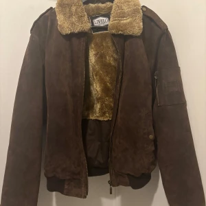 Brun skinnjacka med päls från Livelo Attitude - Säljer en snygg brun skinnjacka från Livelo i storlek 50. Jackan har en mysig pälsfodrad insida och krage, perfekt för kyliga dagar. Den har en dragkedja framtill och långa ärmar. Passar perfekt för höst och vinter. Skicka gärna ett meddelande vid intresse!