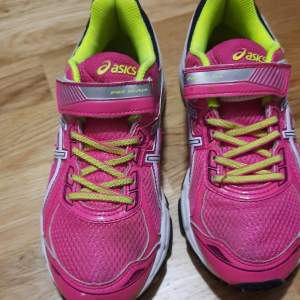 Säljer ett par färgglada Asics sneakers i rosa och gult på innsidan, samt svarta linjer på undersidan. De har snörning och kardborreband för extra bra passform. Skorna är i bra skick med slitstarka sulor och en bekväm passform, de har ett par gångers användning imonhus . Perfekta för träning eller vardagsbruk!