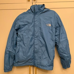Blå vindjacka från The North Face - Säljer en blå vindjacka från The North Face i bra skick. Jackan har en praktisk huva och dragkedja framtill. Perfekt för vår och höst när det blåser lite extra. Materialet är lätt och bekvämt, vilket gör den idealisk för utomhusaktiviteter. Både vind- och vattentät. Strl S.