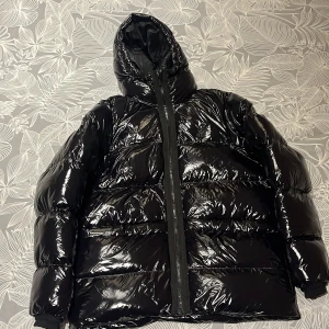 Svart glansig pufferjacka sikslik - Säljer en svart sikslik pufferjacka från Fifth Season. Den är perfekt för kalla dagar med sin tjocka vaddering och har en praktisk huva. Jackan har en dragkedja framtill och är i mycket bra skick. Perfekt för vintern! Storlek medium ny skick. Nypris 1200kr