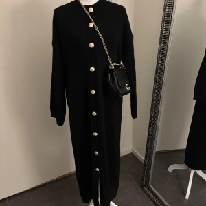 Knitwear Golden Button Dress | Black - Hej! Detta är mitt företag, och du kan köpa produkten här på plick eller via vår hemsida: Nooralanna.com. Det pris som anges är fast, och jag kommer inte att svara på meddelanden om budgivning. Tack för förståelsen! 	•	Färg: Svart 	•	Längd: 133 cm       •     Kan öppnas och användas som cardigan 	•	Lagerstatus: 3 st kvar  Retur gäller endast via beställning på hemsidan. Läs retur policy vad som gäller.   Kontakta mig gärna vid seriösa frågor eller köp. Tack!