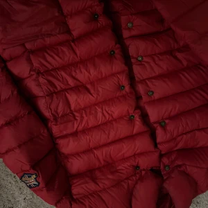 Röd dunjacka från Newhouse - Säljer en snygg röd dunjacka från Newhouse. Jackan har en quiltad design med knappar och är perfekt för kyliga dagar. Den har en cool patch med brittisk flagga på ärmen. Perfekt för höst och vinter!