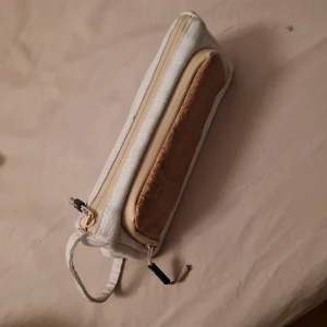 Fint pennskrin  - Säljer en praktisk beige, vit penskrin med dragkedja. Den har flera fack och elastiska band för att hålla saker på plats. Perfekt för pennnor, sudd osv . Den är i bra skick utan för men inut i är den lite smutsig men inget är trasigt
