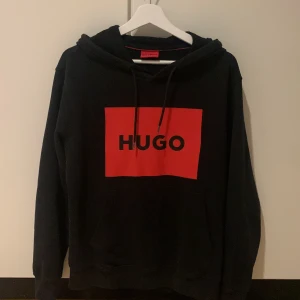 Hugo hoodie svart/röd - Säljer en snygg svart hoodie från Hugo med en stor röd logga på bröstet.