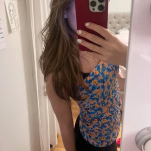 Blommig kortkjol - Säljer en superfin blommig kortkjol i blått och orange. Kjolen är tight och perfekt för sommaren. Den har ett färgglatt mönster som verkligen sticker ut. Perfekt för både vardag och fest! Den är från Pull&Bear i storlek xs. Kan även användas som en gullig topp🌸🌺