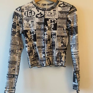 Svartvit tröja med tidningsmönster - Tröjan är långärmad och har en tight passform, perfekt för att sticka ut i mängden. Materialet är mjukt och stretchigt, vilket gör den bekväm att bära. Passar perfekt för höst och vår!