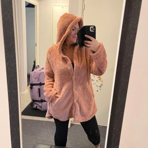 Rosa teddyjacka med huva - Mysig rosa teddyjacka med huva och knappar framtill. Perfekt för kyliga dagar när du vill vara både varm och stilren. Jackan har en avslappnad passform och är supergosig! Helt ny