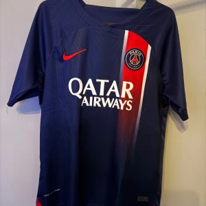 Blå PSG fotbollströja - Säljer en snygg blå PSG fotbollströja från Nike. Den har korta ärmar och ett coolt mönster med röda och vita detaljer. Perfekt för alla fotbollsfans som vill visa sitt stöd för laget. Tröjan är i bra skick och redo för nästa match!självklart äkta nypris 1199 mitt pris 329