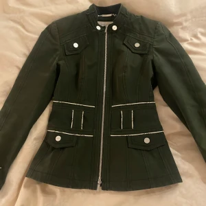 Grön jacka med dragkedja Karen Millen - Snygg grön jacka i bra skick med dragkedja och knappar. Den har en figursydd passform och långa ärmar. Perfekt för höst och vår! 🧥