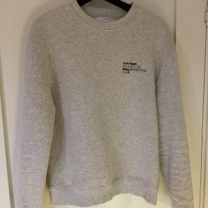 Grå sweatshirt från Axel Arigato - Säljer en stilren grå sweatshirt från Axel Arigato i storlek M. Tröjan är i mycket bra skick och har en klassisk rund halsringning. Perfekt för både vardag och avslappnade tillfällen. Tillverkad i Portugal med högkvalitativt material för bästa komfort.
